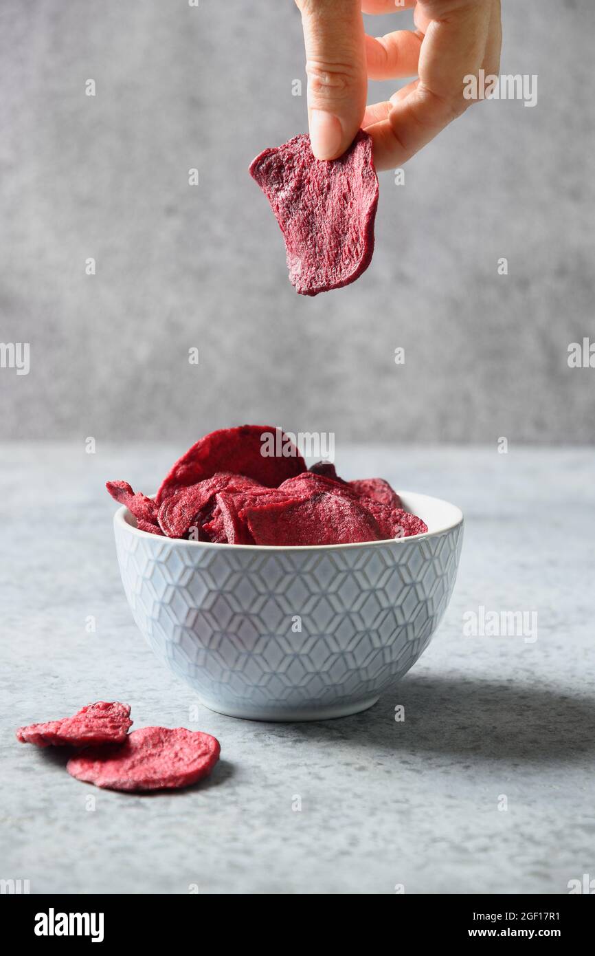 Vegetable beetroot chips in hand on a gray background. Vegan snack. Close up. Vertical format. Stock Photo