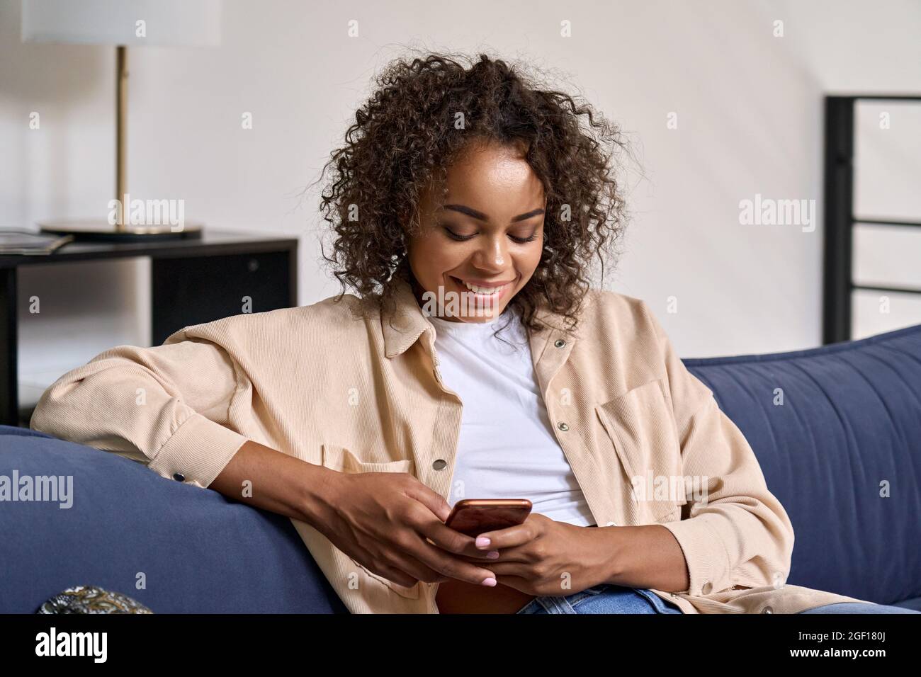 Happy African American girl using cell phone relaxing on couch at home ...