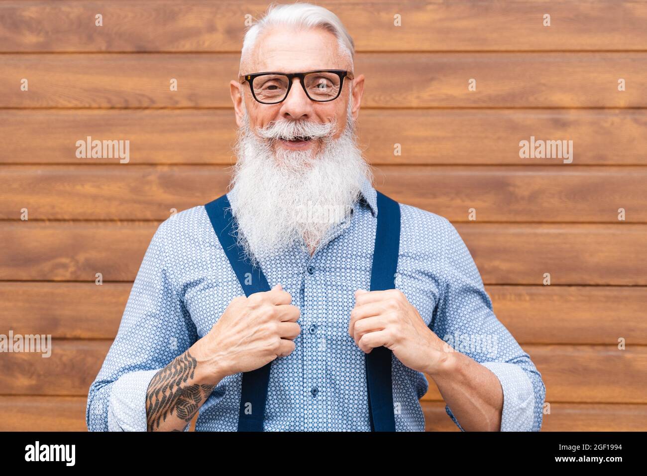 Happy hipster senior man smiling on camera with wood wall in background outdoor in the city- Focus on face Stock Photo