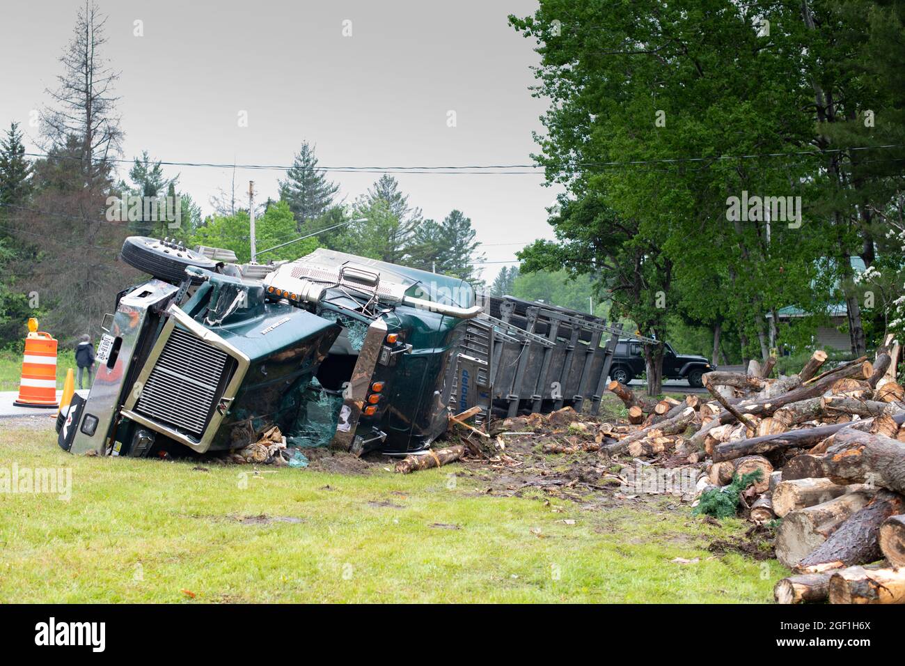 A log hauling truck accident in Hoffmeister, NY USA involving a logging truck rolling on its side and dumping a load of logs on the front of a house. Stock Photo