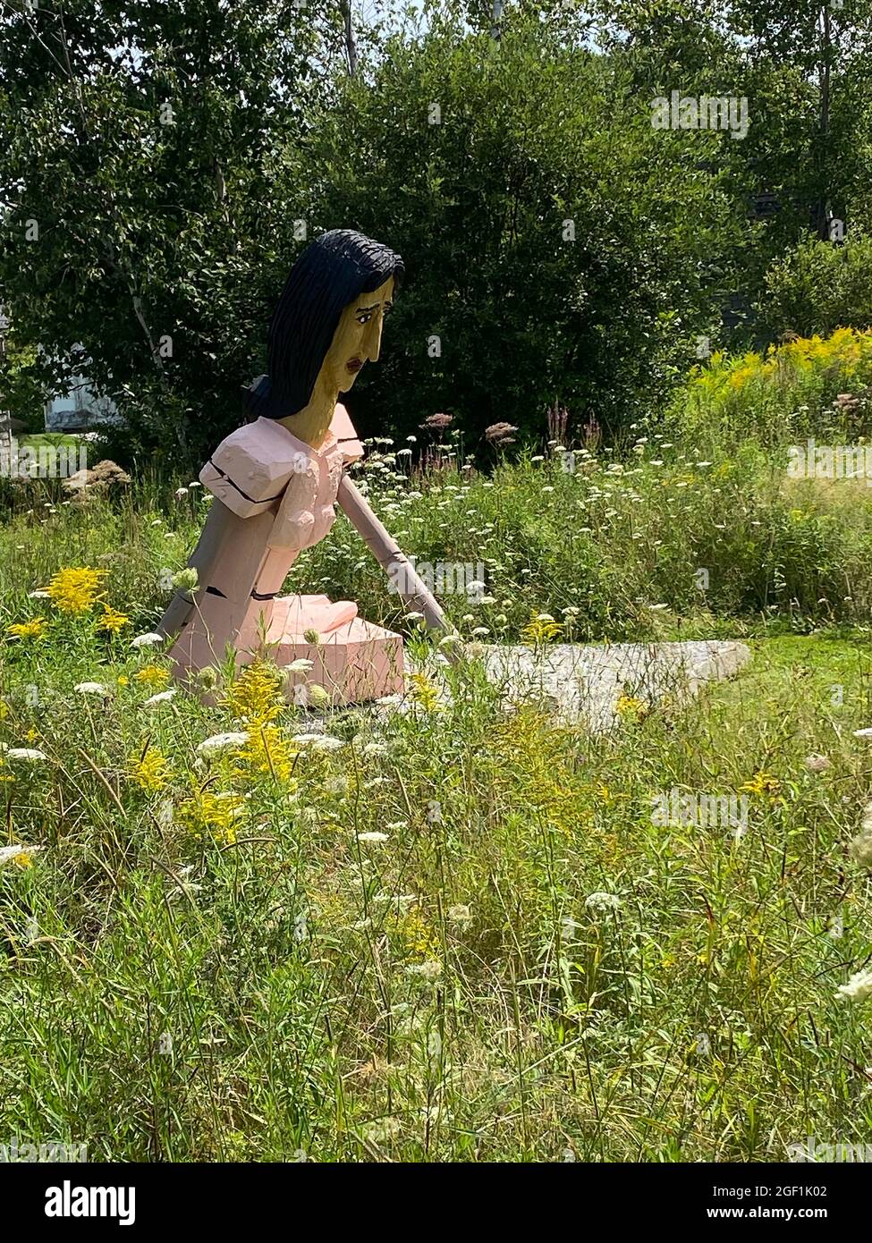 This sculpture, titled Local Girl, was done by American artist Bernard Langlais and is housed at the Langlais Sculpture Preserve in Cushing, Maine. It is based on Christina Olson, who is is best known as the subject of N C Wyeth’s Christina’s World painting. In the background is a cow by Langlais.  Bernard Langlais (1921 - 1977) was a Maine native and maintained a studio in Cushing, Maine until his death at the age of 56. He developed his artistic interest at the Corcoran School of Art in Washington DC and the Skowhegan School of Painting and Sculpture. Stock Photo