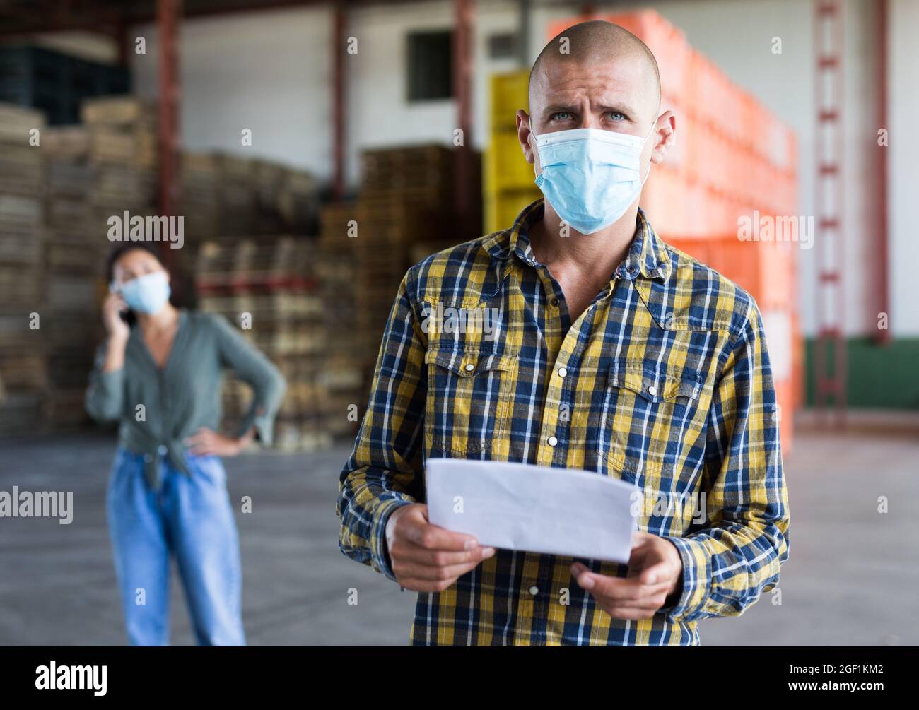 Male manager in protective mask with documents inside warehouse Stock Photo