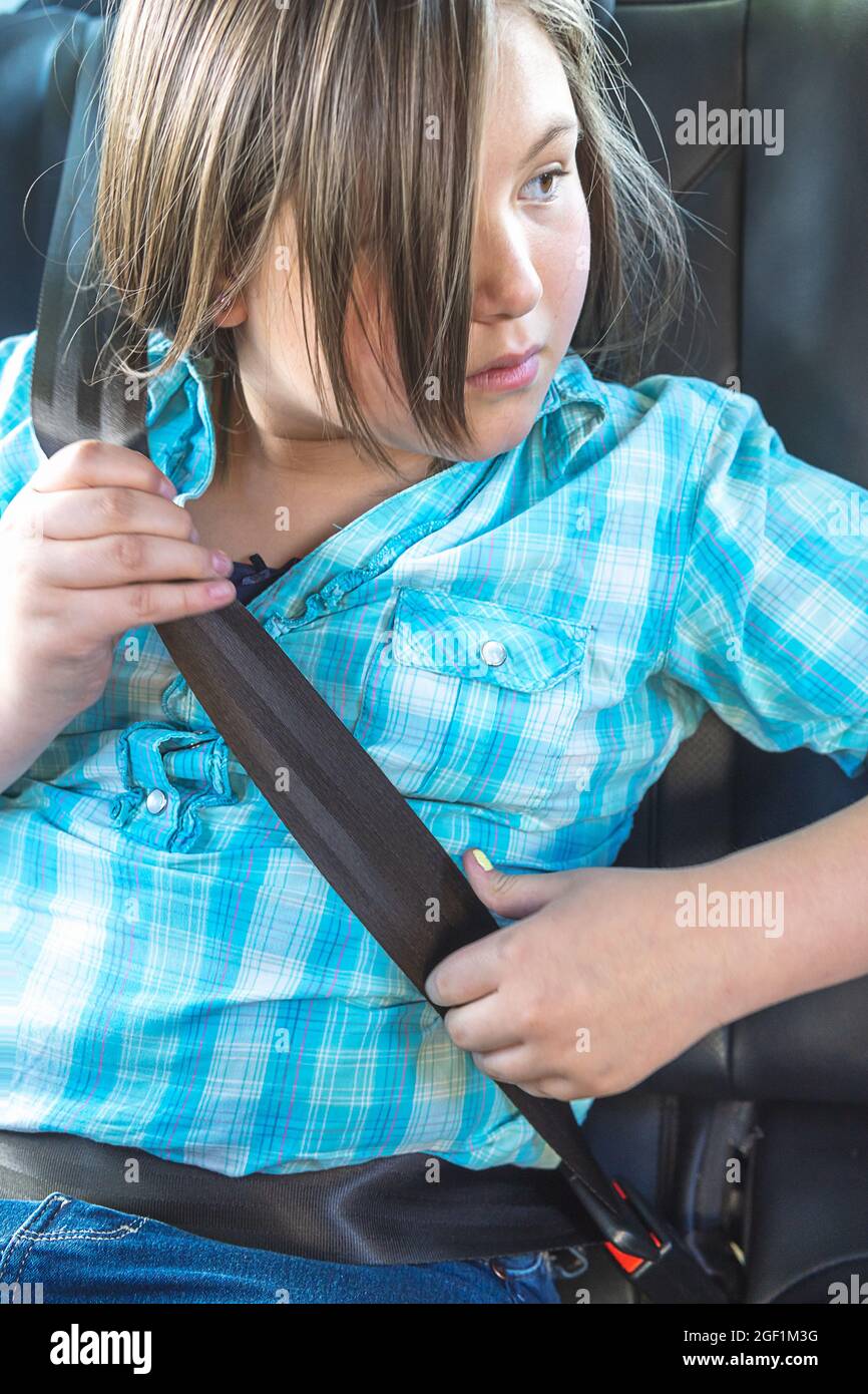 Blonde girl putting on a seat belt in the back seat of a car Stock