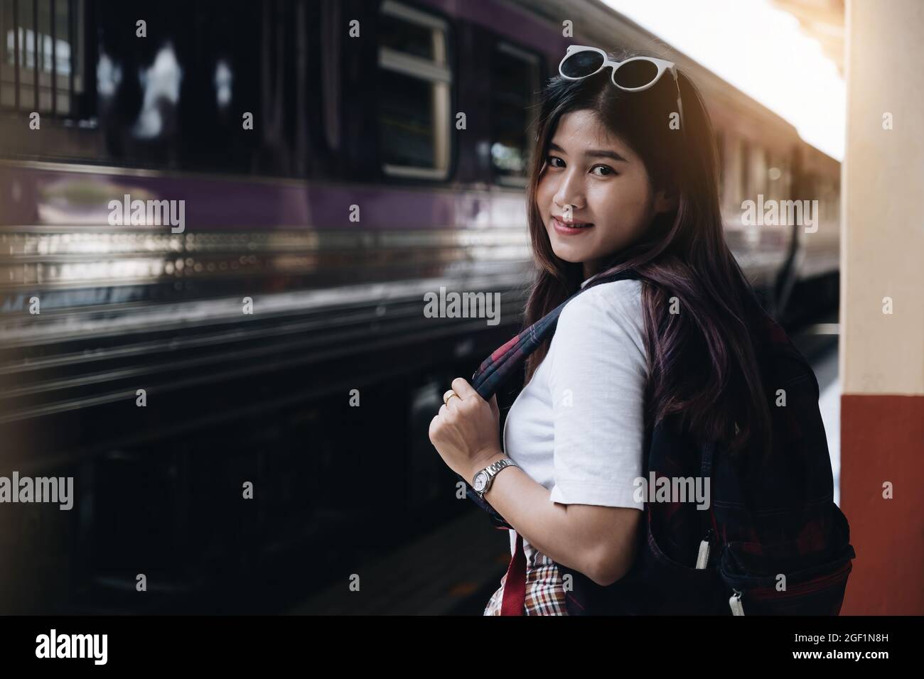 Image of a woman with a rucksack standing at a train station waiting to board a train. concept of solo travel. Stock Photo