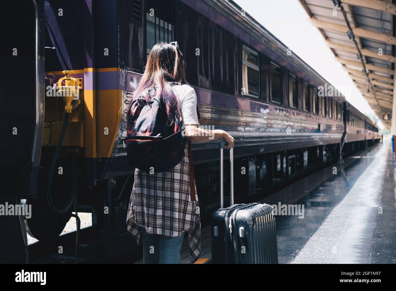 Image of a woman with a rucksack standing at a train station waiting to board a train. concept of solo travel Stock Photo