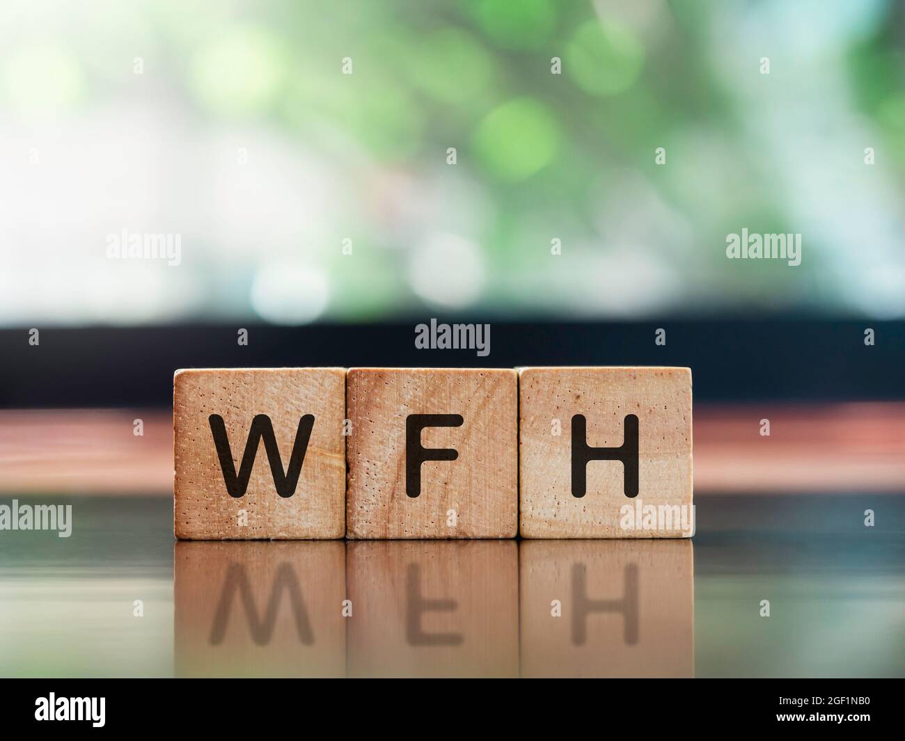 Work from home concept. WFH, words on wooden cube blocks on brown wood desk and green nature background with copy space. Stock Photo