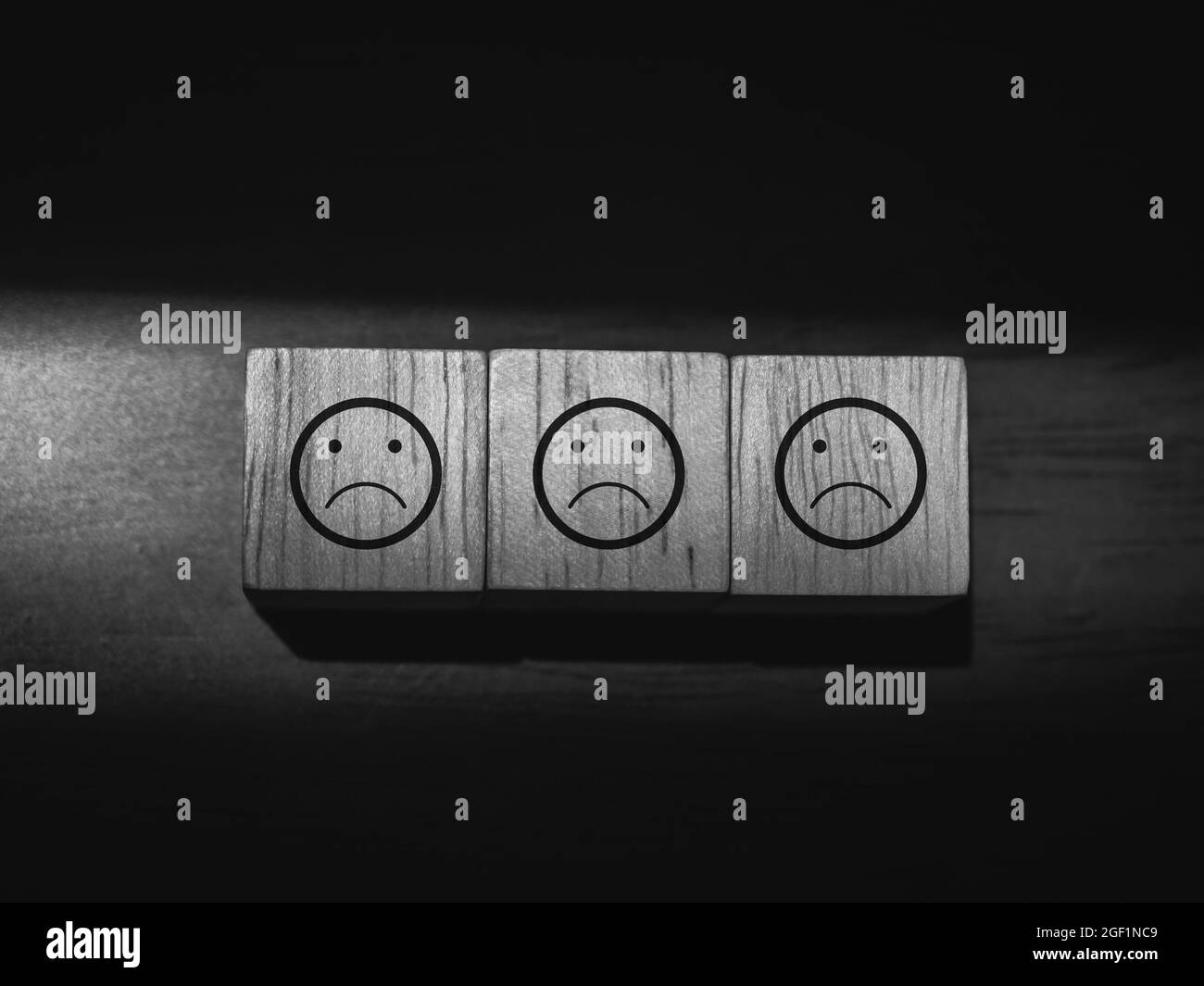 Sad, boring face emoticon on wooden cube blocks on dark background, black and white style. Not satisfied, feedback review, satisfaction service concep Stock Photo