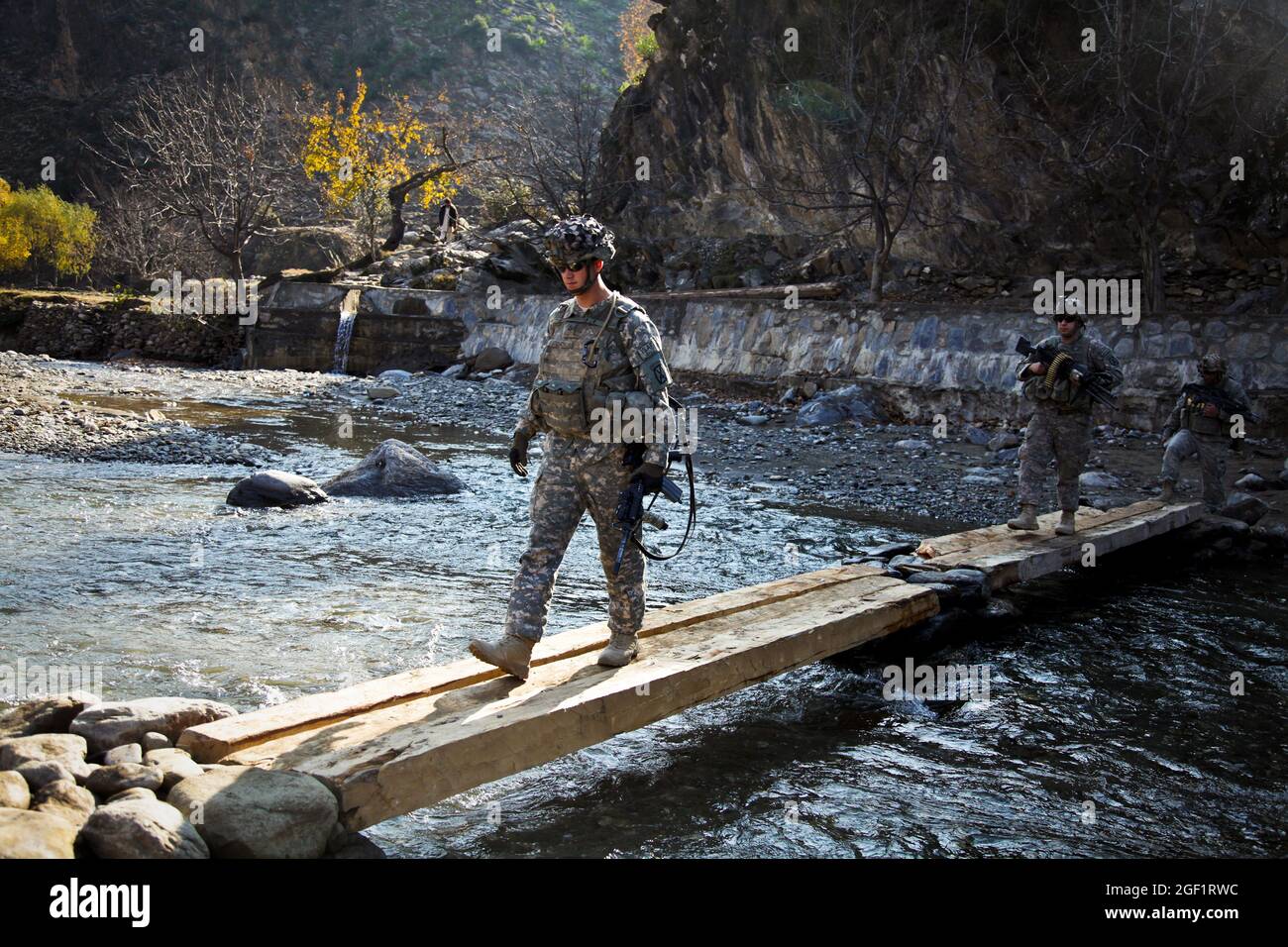 U.S. Army Pfc. Christian Leach, 21, from Columbus, Ohio, and fellow Soldiers assigned to Combat Company, 1st Battalion, 32nd Infantry Regiment, 3rd Brigade Combat Team, 10th Mountain Division, cross a river as they approach the village of Lachey in the Shigal district of Kunar province, Afghanistan on Dec. 7. Stock Photo