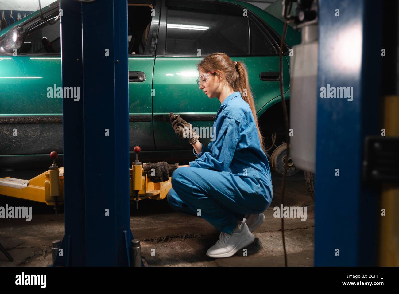 Portrait of a woman auto mechanic in working overalls and glasses. holding a nut in his hands. Baner Stock Photo