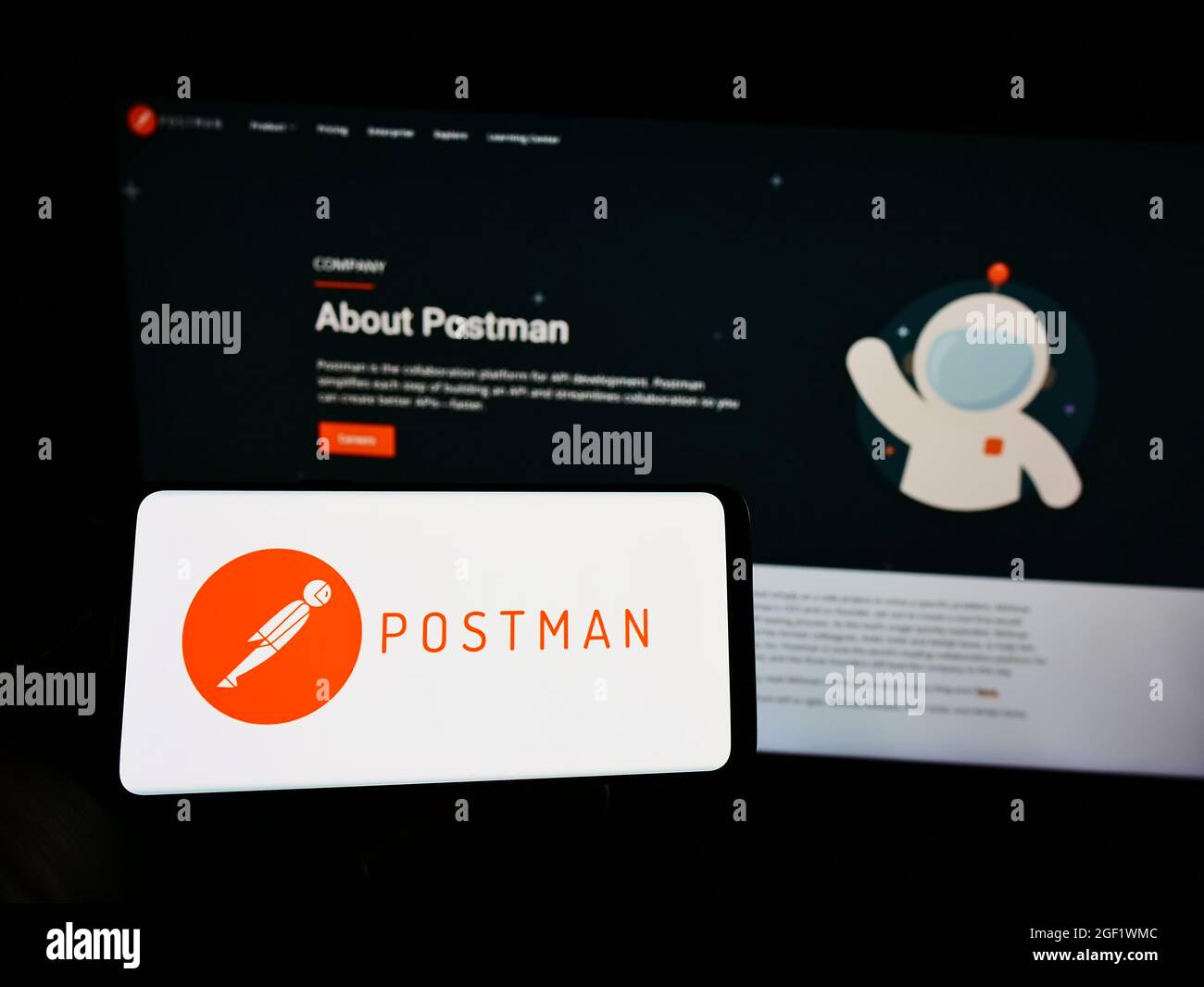 Person holding mobile phone with logo of US collaboration platform company Postman Inc. on screen in front of web page. Focus on phone display. Stock Photo