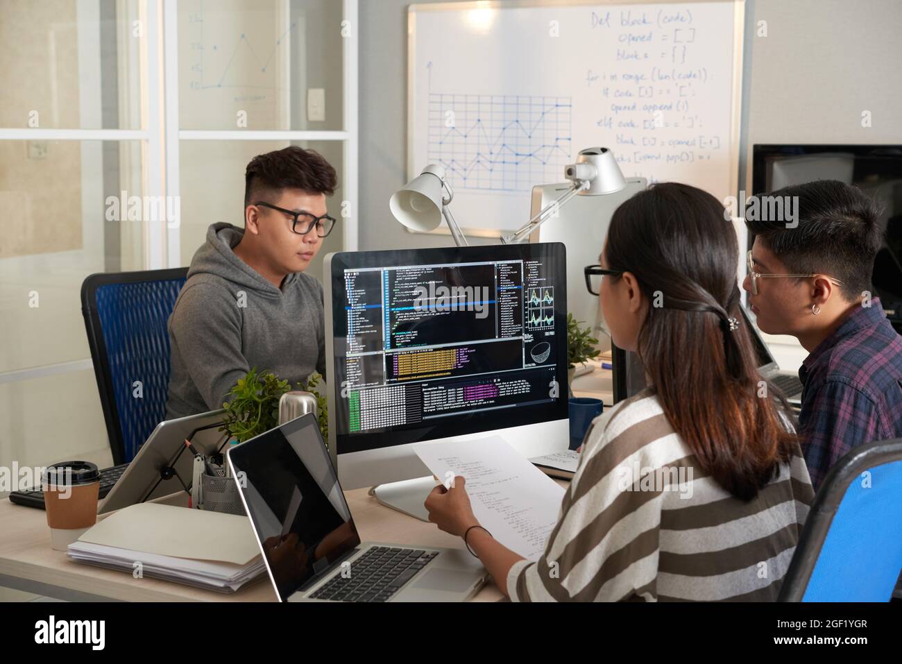Young woman checking programming code on computer screen and comparing ...