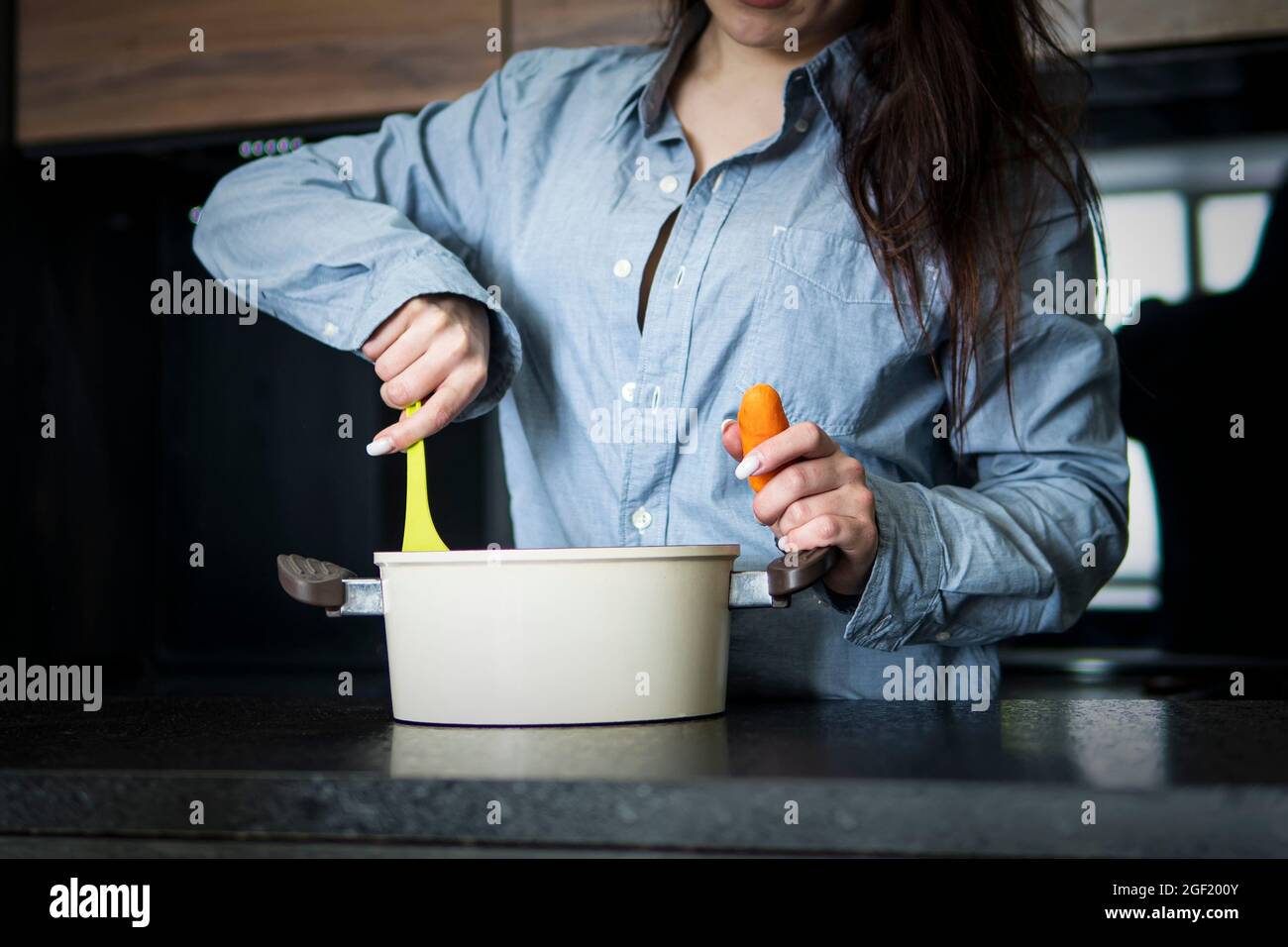 Cooking woman in kitchen with spoon. A young wife cooks borscht in the kitchen interior. Stock Photo