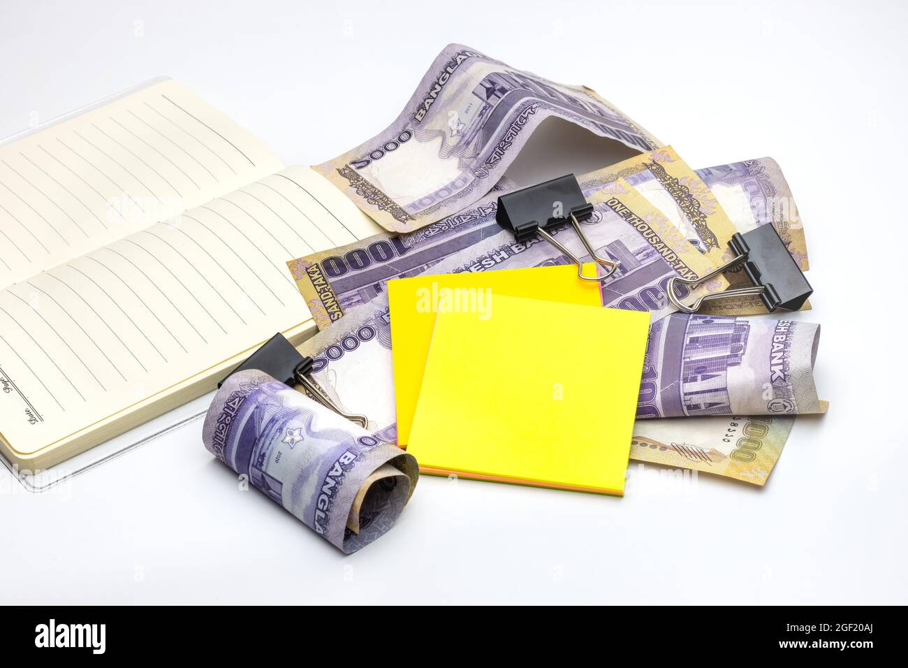 Scattered thousand taka bangladesh banknotes with a notebook, black binder, and sticky notes on white background Stock Photo