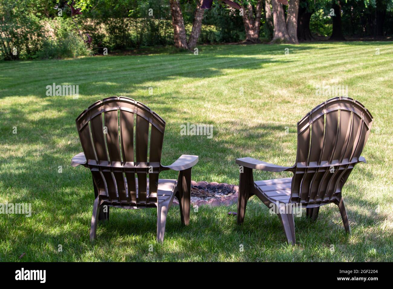 Close up backside view of a pair of gray lawn chairs facing a fire pit, in a back yard with light shade Stock Photo