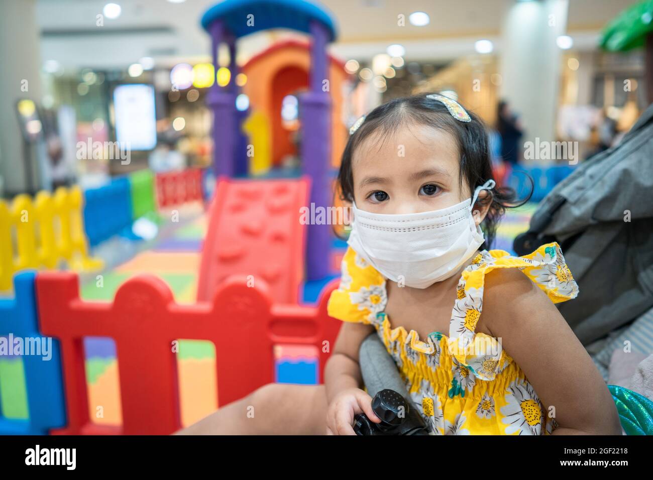 Southeast Asian female kid wearing a facemask at the playground in the mall Stock Photo