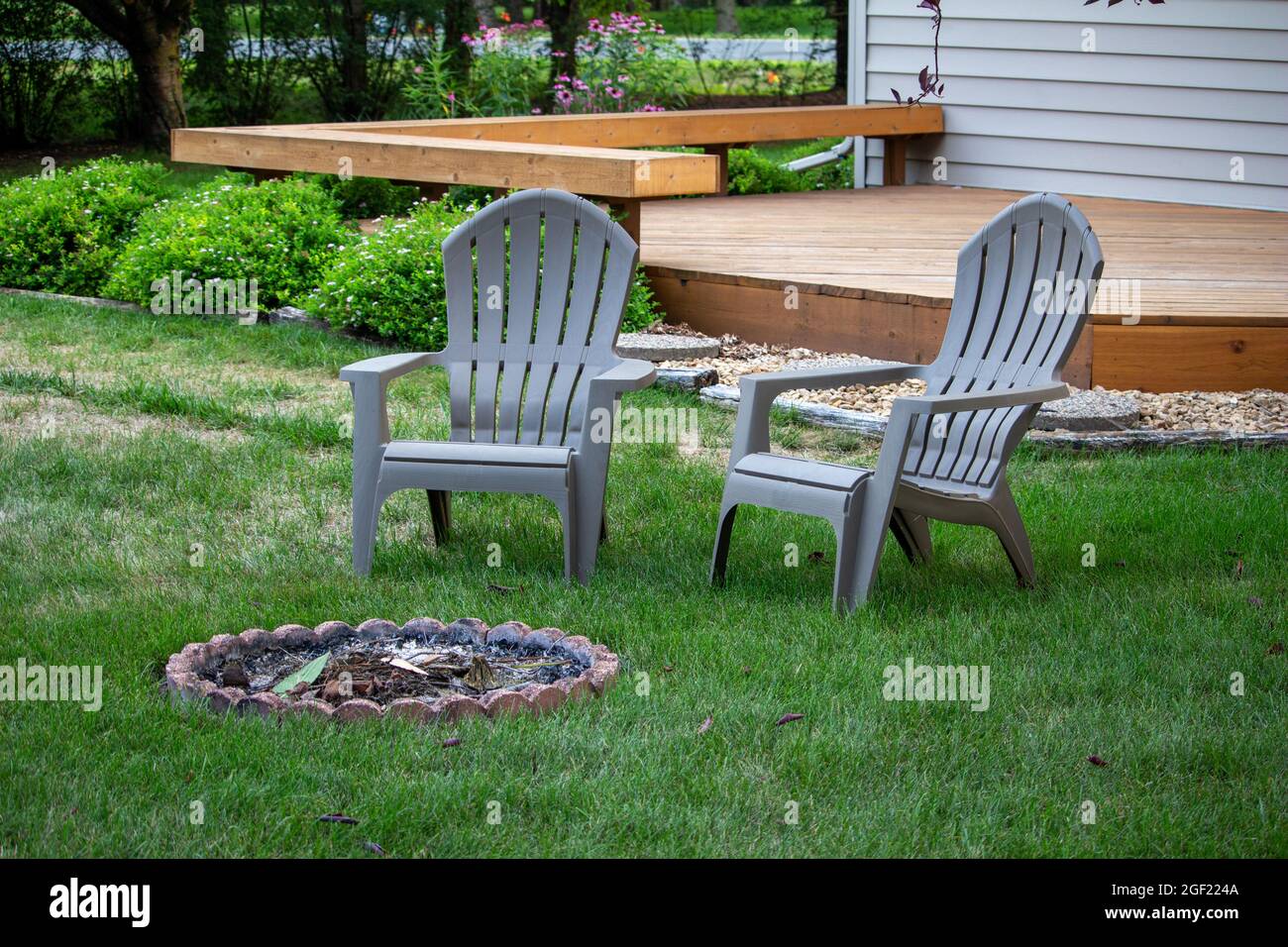 Close up view of a pair of gray lawn chairs facing a fire pit, in a back yard with deck in background Stock Photo