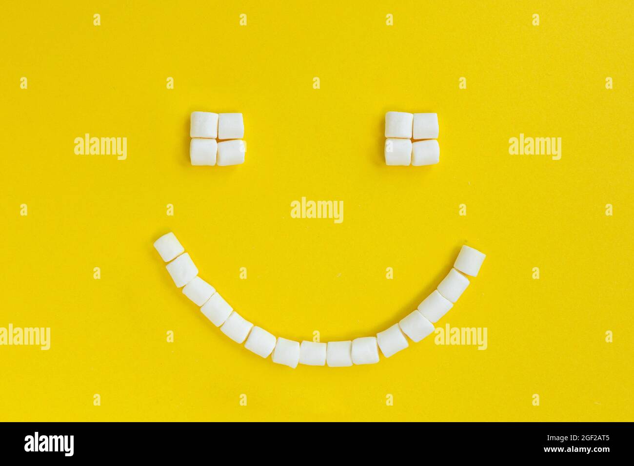 smiling face of white marshmallows on yellow background, holiday card, top view, food and lifestyle concept Stock Photo