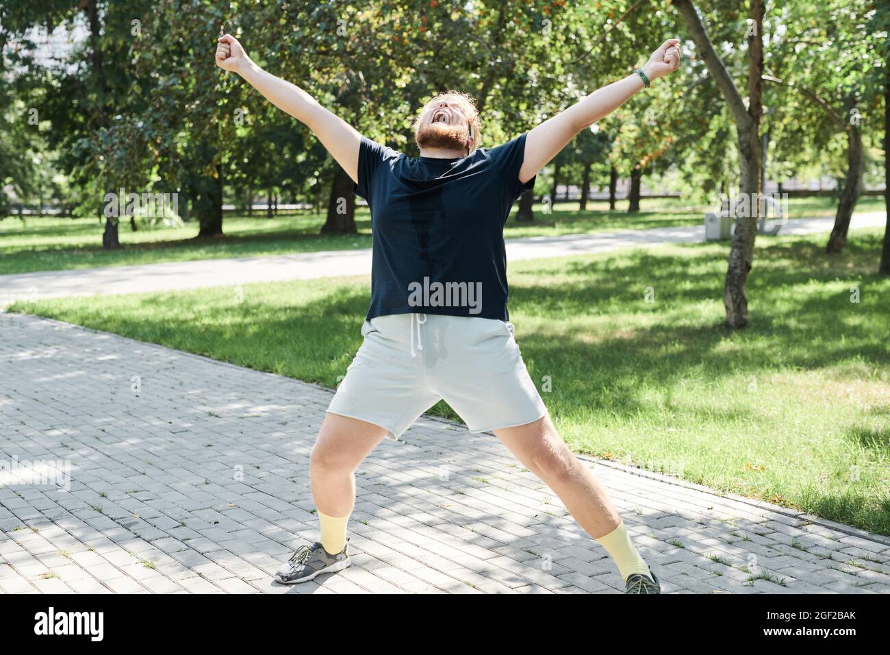 Overweight man training outdoors he standing with his arms up and happy with his good results Stock Photo