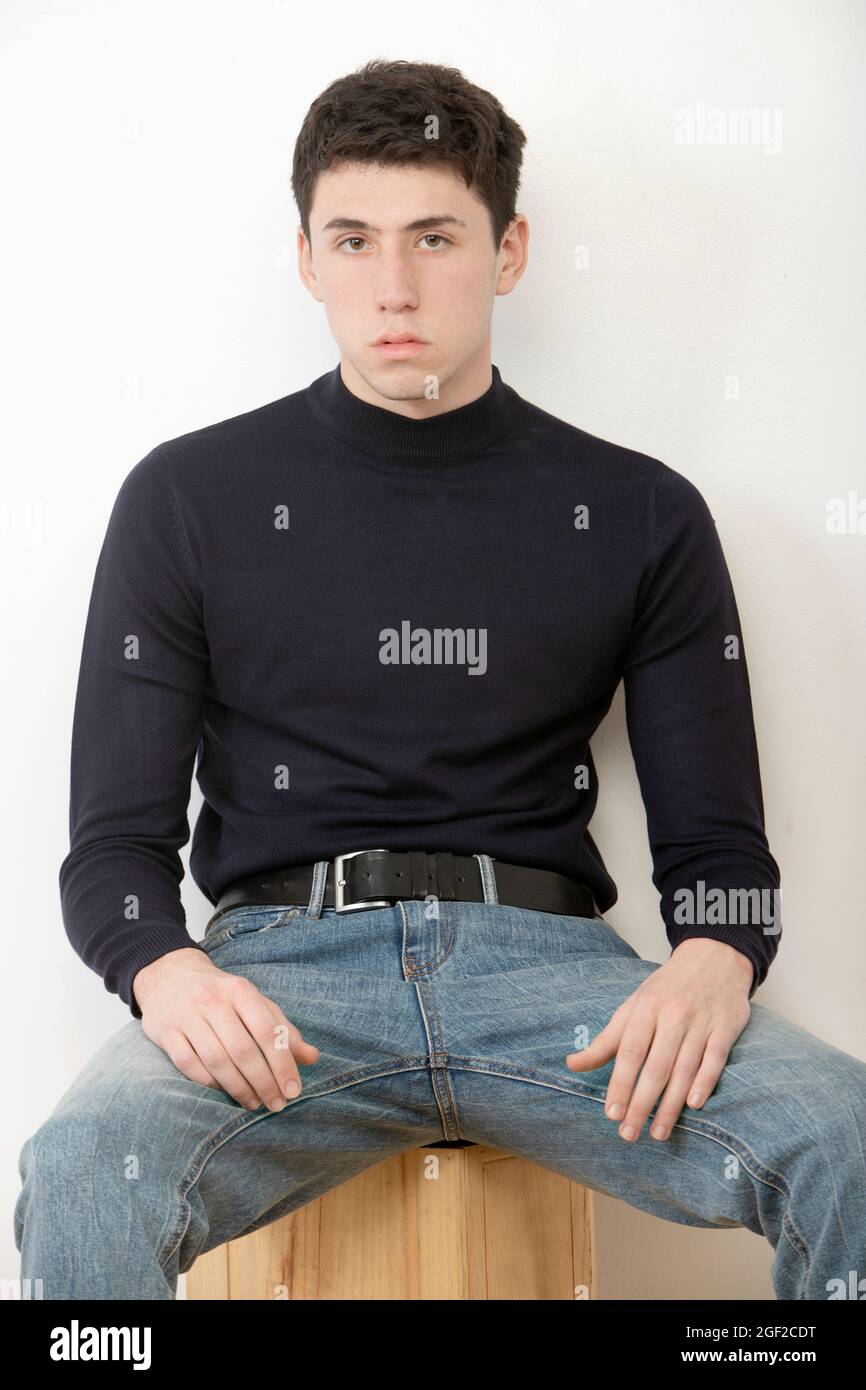 handsome caucasian dark haired guy looking at camera with serious expression sitting with turtleneck sweater Stock Photo