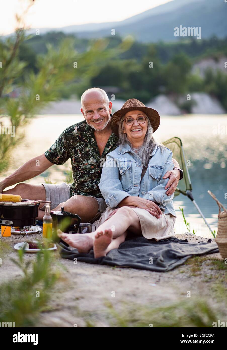 Happy senior couple resting on summer holiday trip, barbecue by lake. Stock Photo