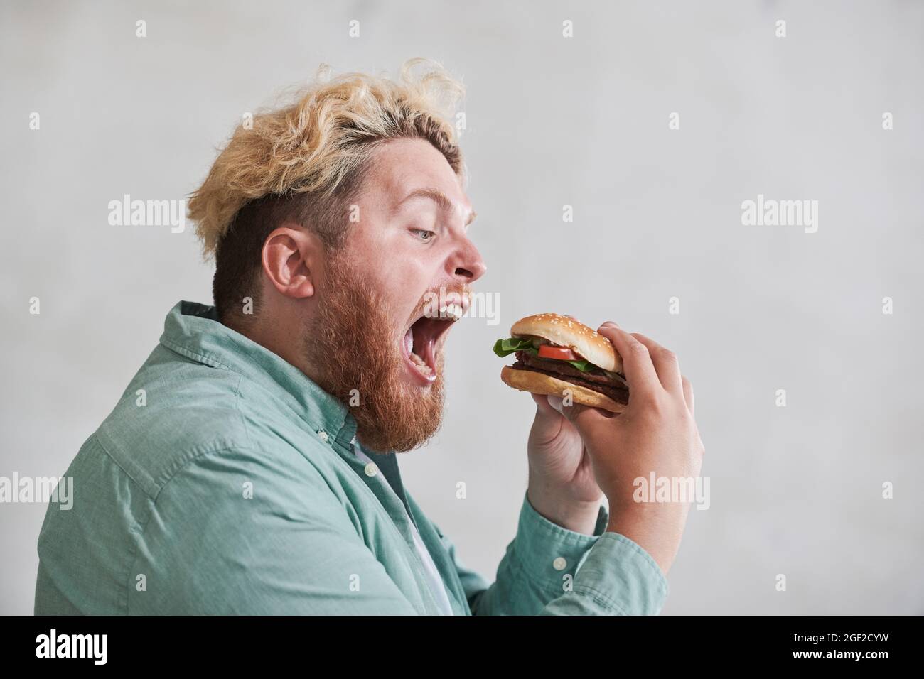 Overweight man opening his mouth and eating fast food against the white background Stock Photo