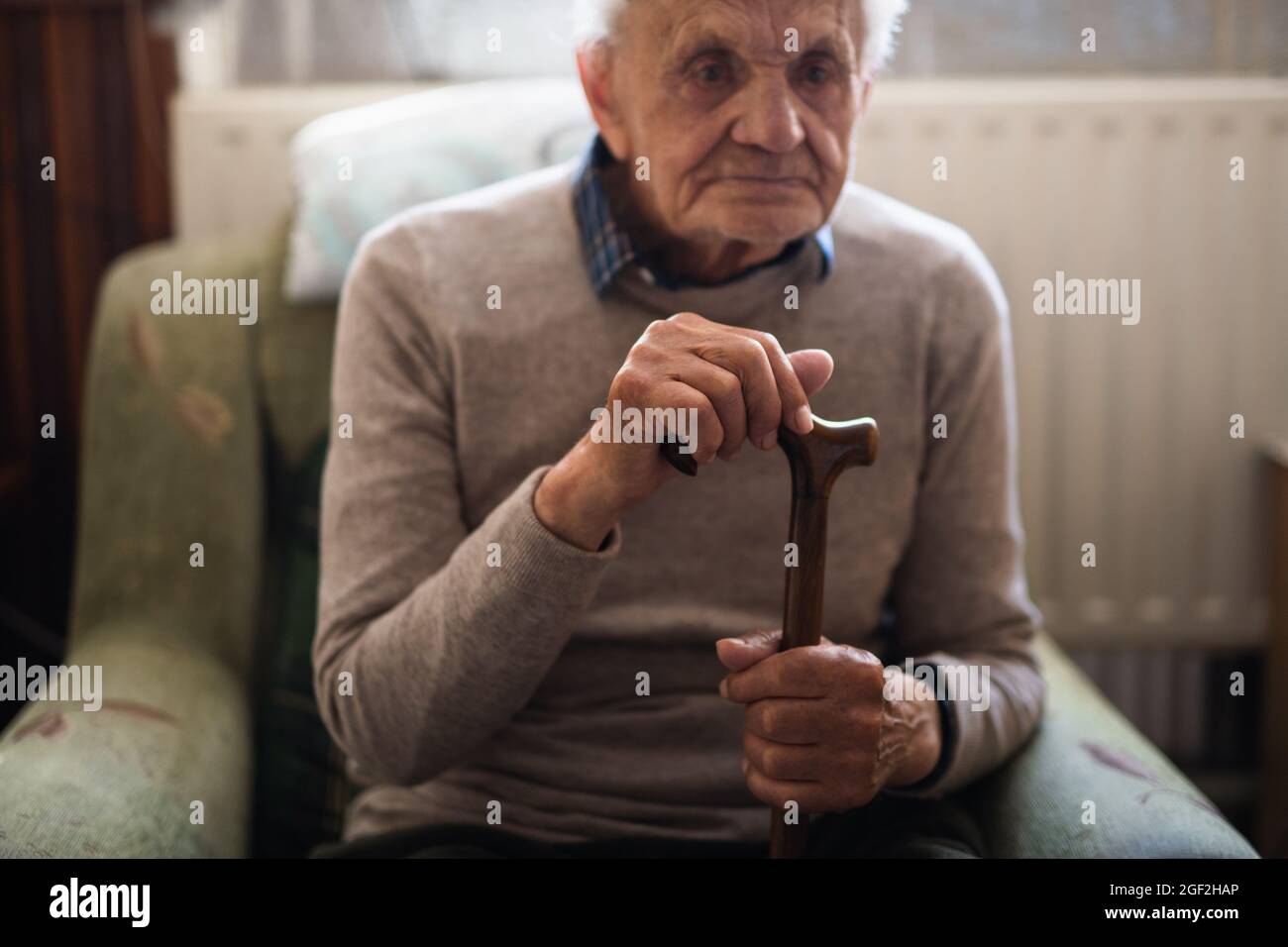 Sad elderly man with walking stick sitting on armchair indoors at home, resting. Stock Photo