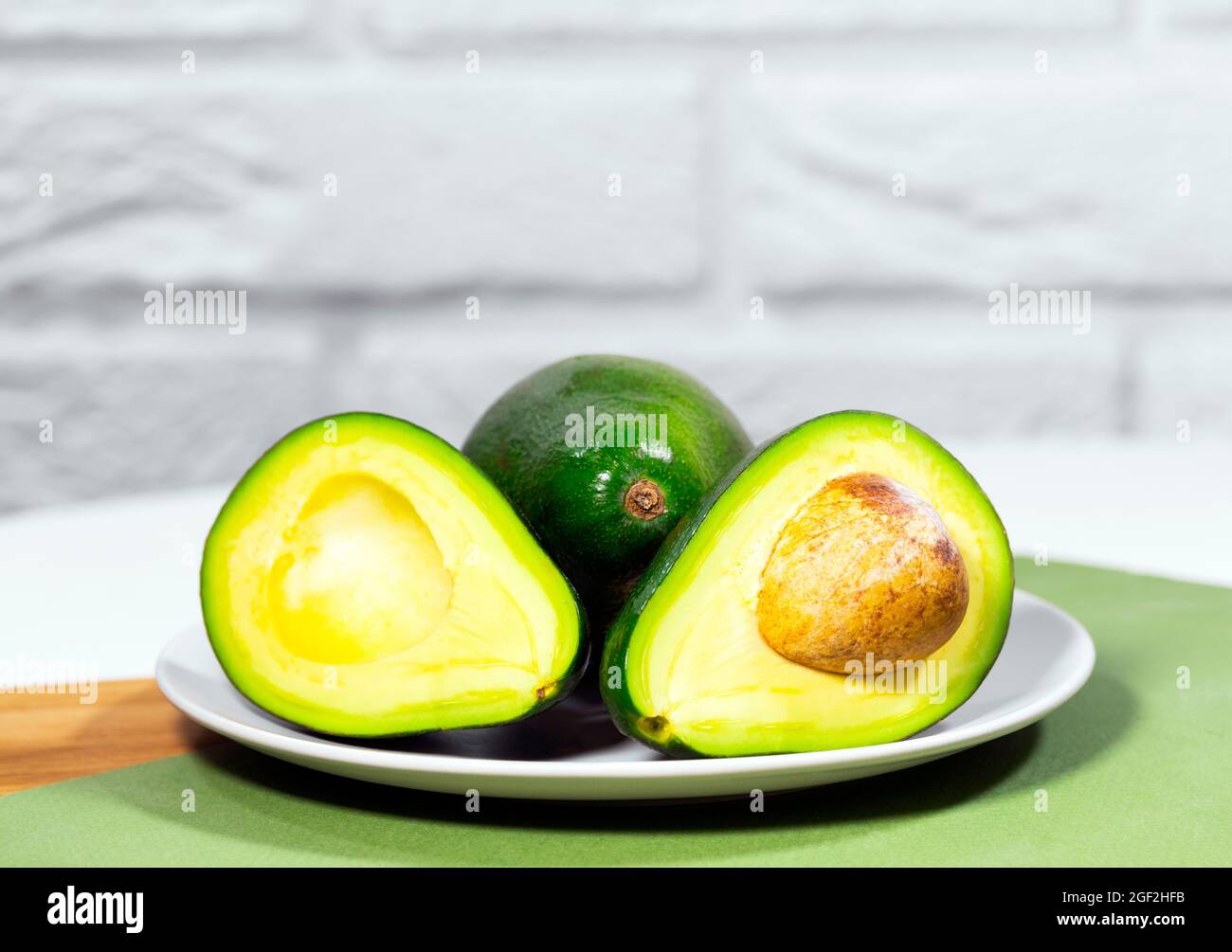 Halves of Ripe Avocado on plate served on table, Green and white background, Healthy oily food, Keto diet, Close up Stock Photo
