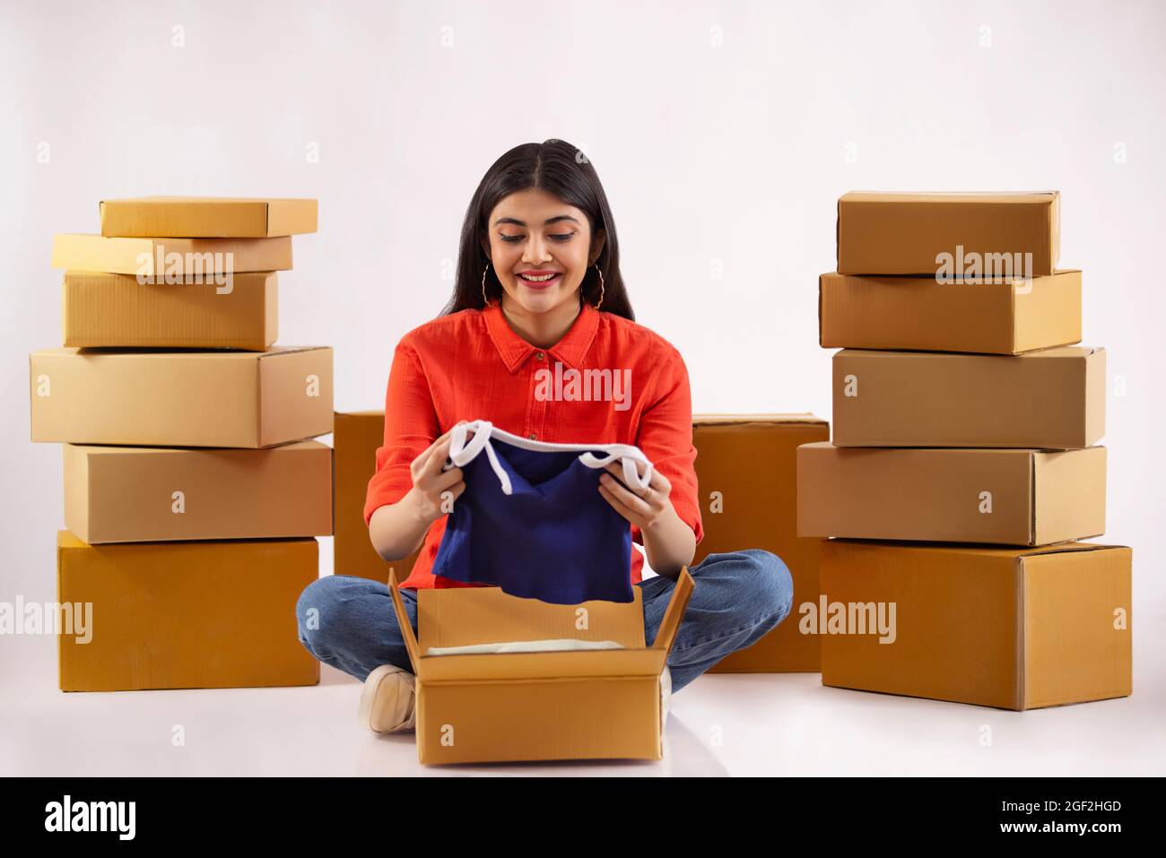 A young woman unpacking new dress sitting amidst cardboard boxes. Stock Photo