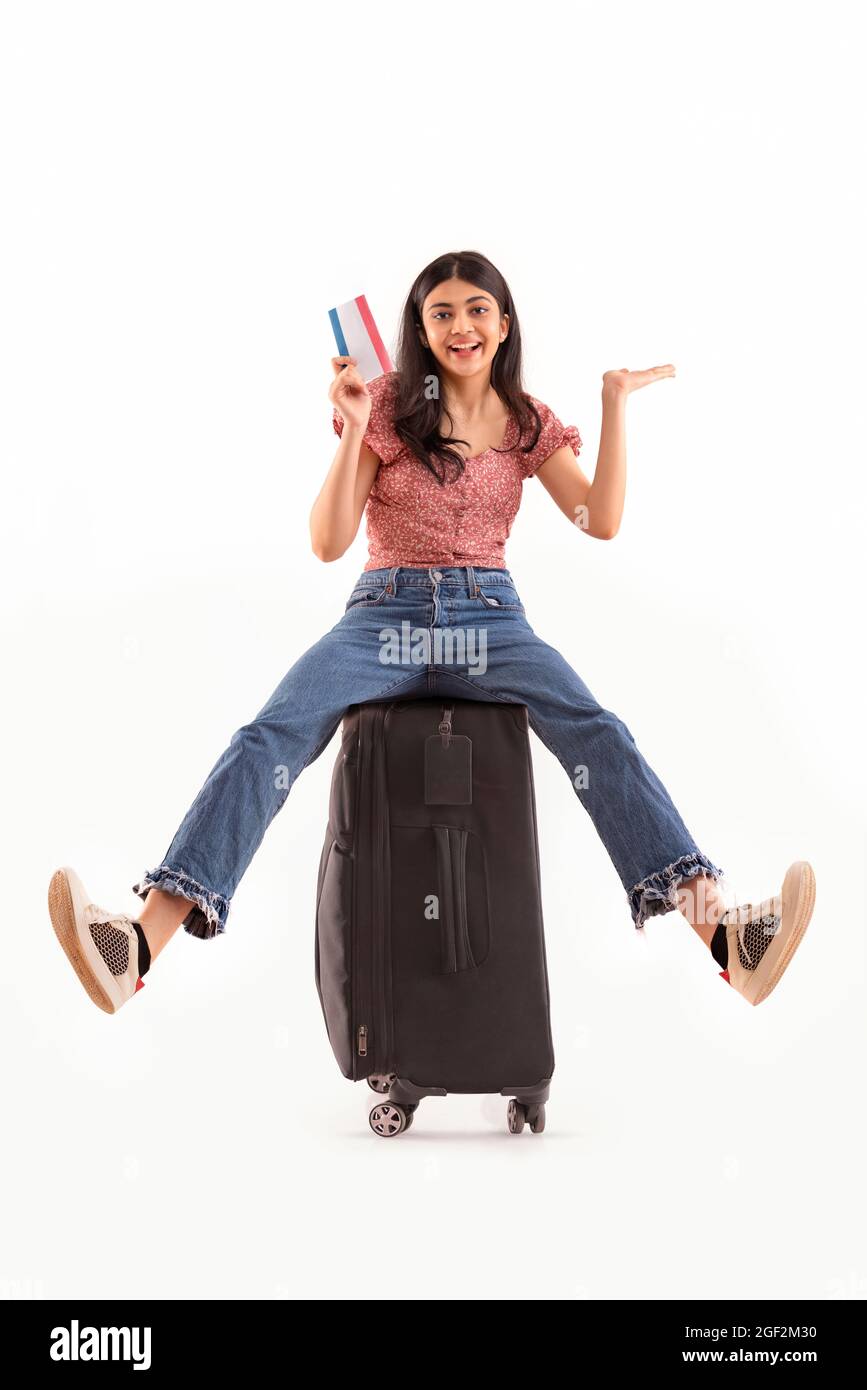 An excited woman sitting on her luggage holding air travel ticket. Stock Photo