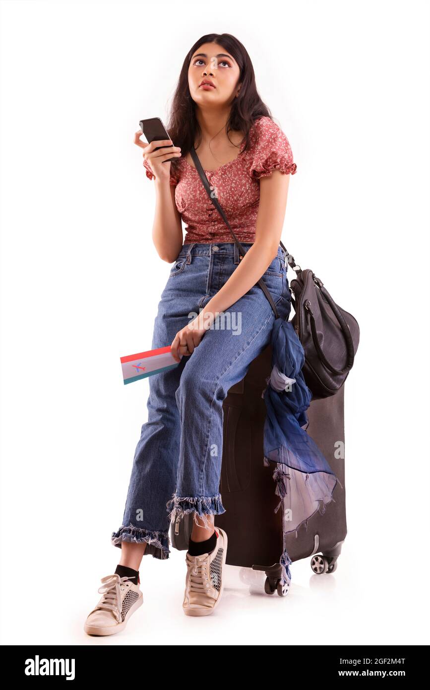 A young woman with an exhausted expression booking an online travel ticket on mobile phone. Stock Photo