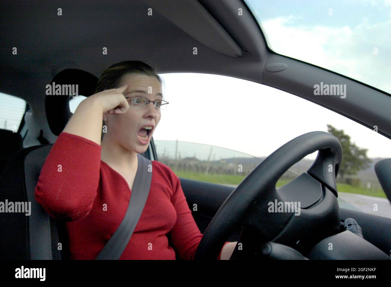 female car driver is frightened and tapping one's forehead at somebody, Germany Stock Photo