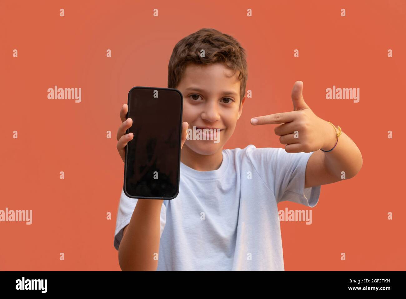Young caucasian little boy showing a smartphone display screen. Useful for layout app or website advertisement. Looking at camera. Stock Photo