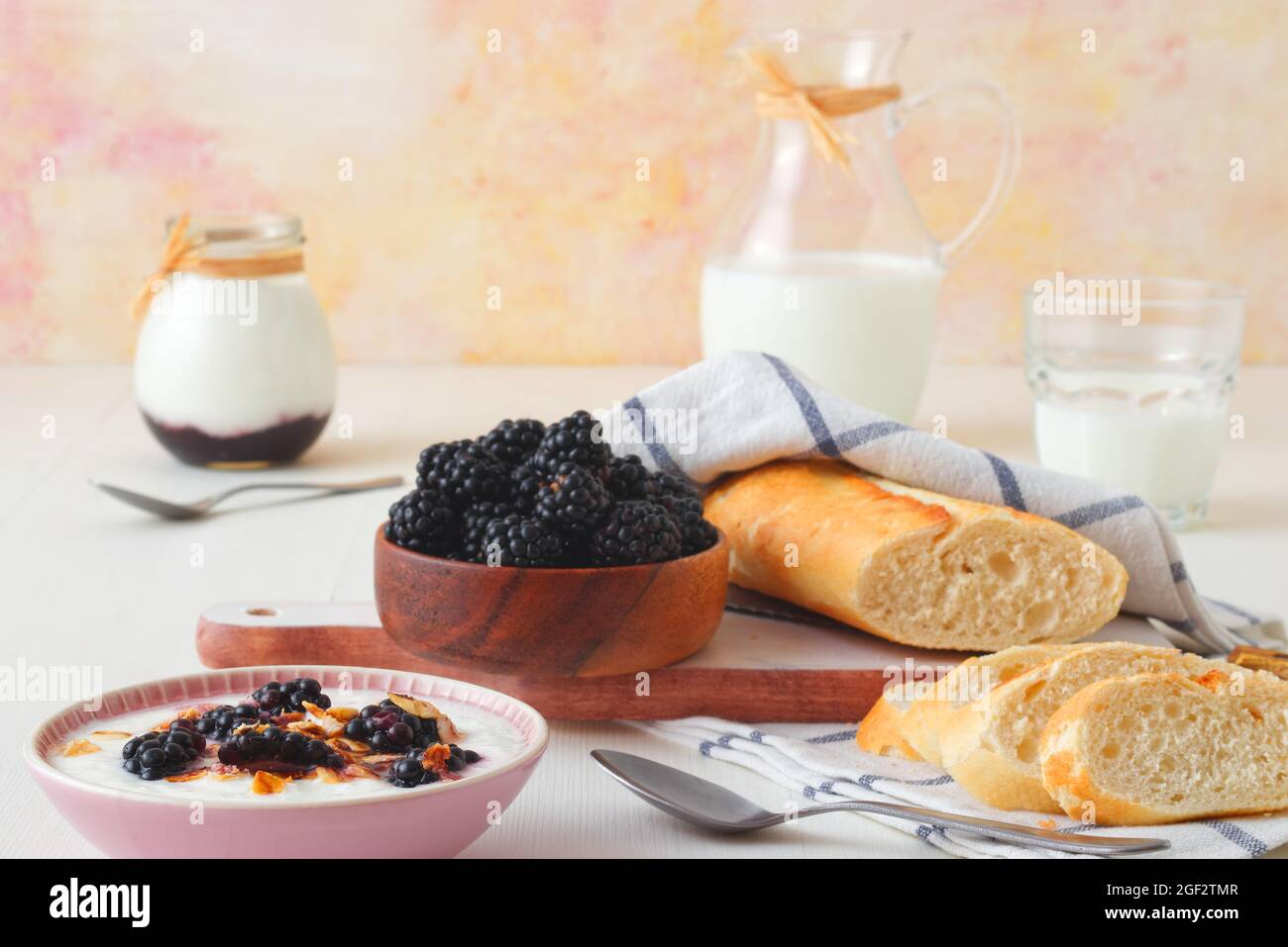 Bowl of blackberries, milk, yoghurt with oatmeals and bread, a table set for breakfast, ingredients from the local farmers market. Closeup, front view Stock Photo