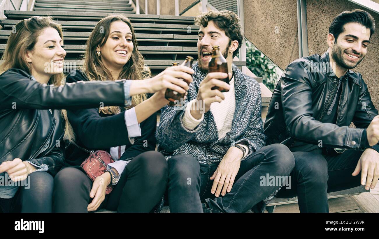 group of gen z young friends toasting with beers. Young people having fun raising bottled beers. Alcohol consumption concept. Stock Photo