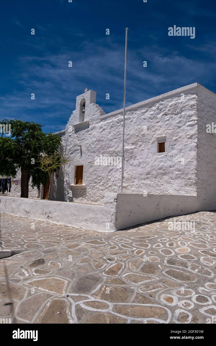 Old small chapel with trees in yard religious destination at Kimolos island Chora Cyclades Greece. Whitewashed Orthodox Church with belfry and cross e Stock Photo