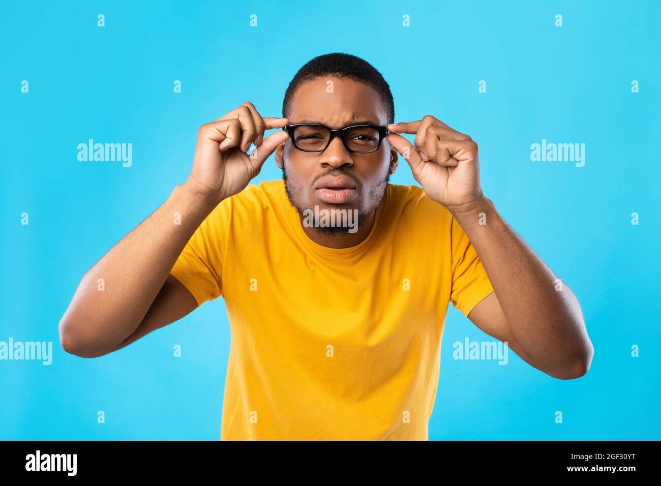 African American Guy With Poor Eyesight Squinting Eyes, Blue Background Stock Photo