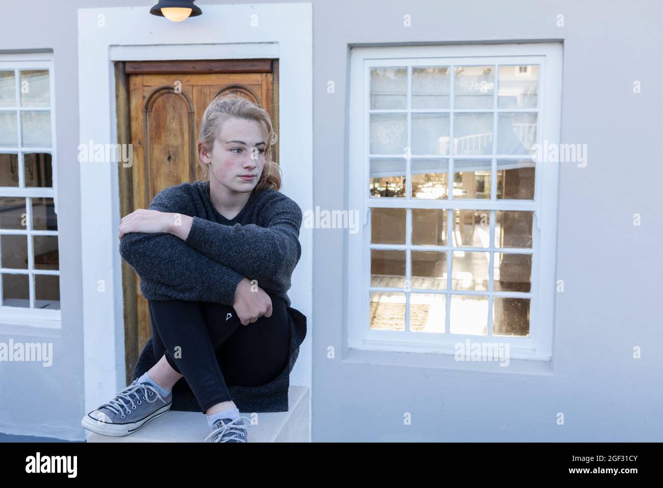 Teenage girl sitting cross legged on a low wall outside a house Stock ...