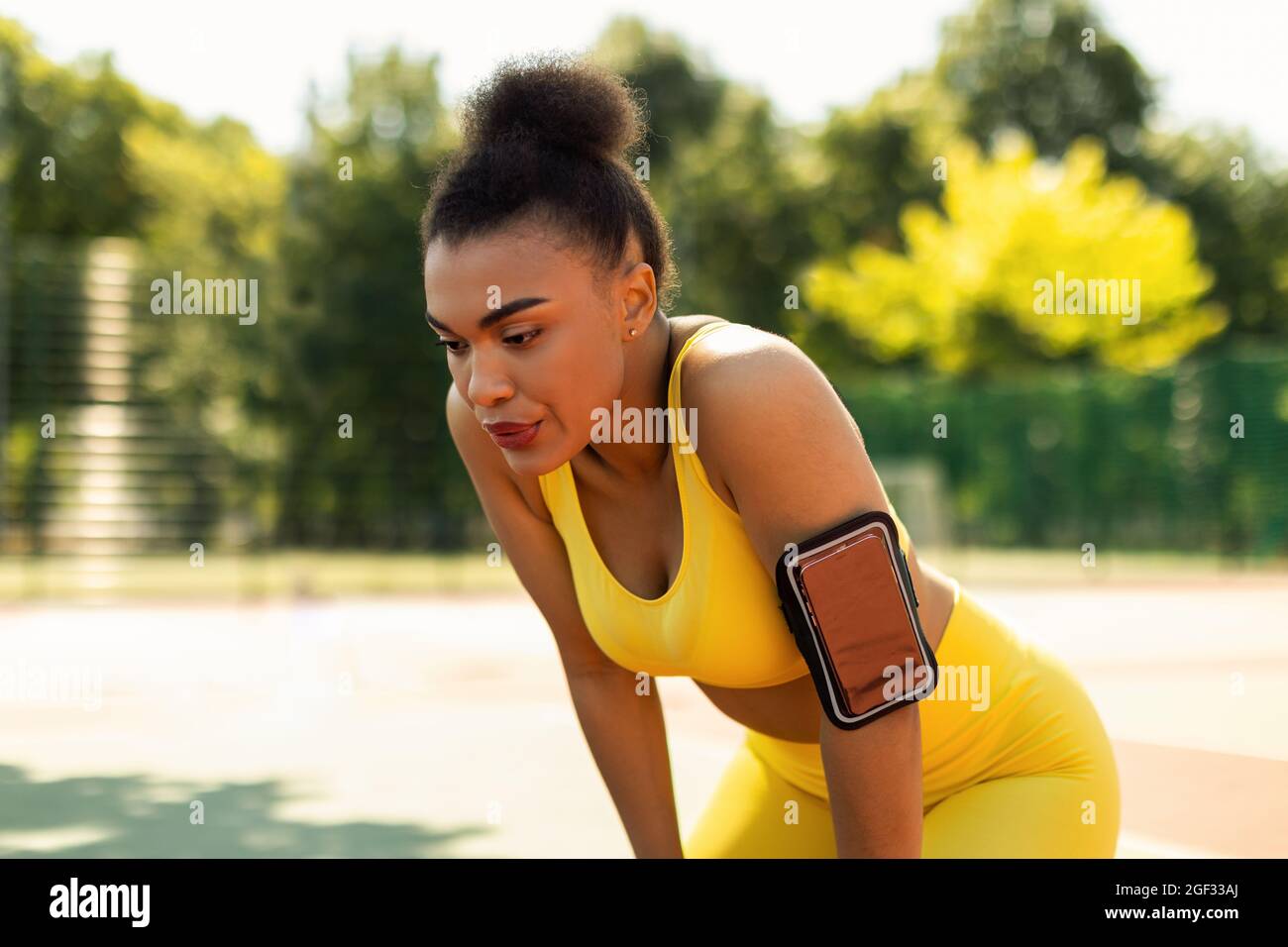 Sporty black woman in yellow sportswear resting after run Stock Photo ...