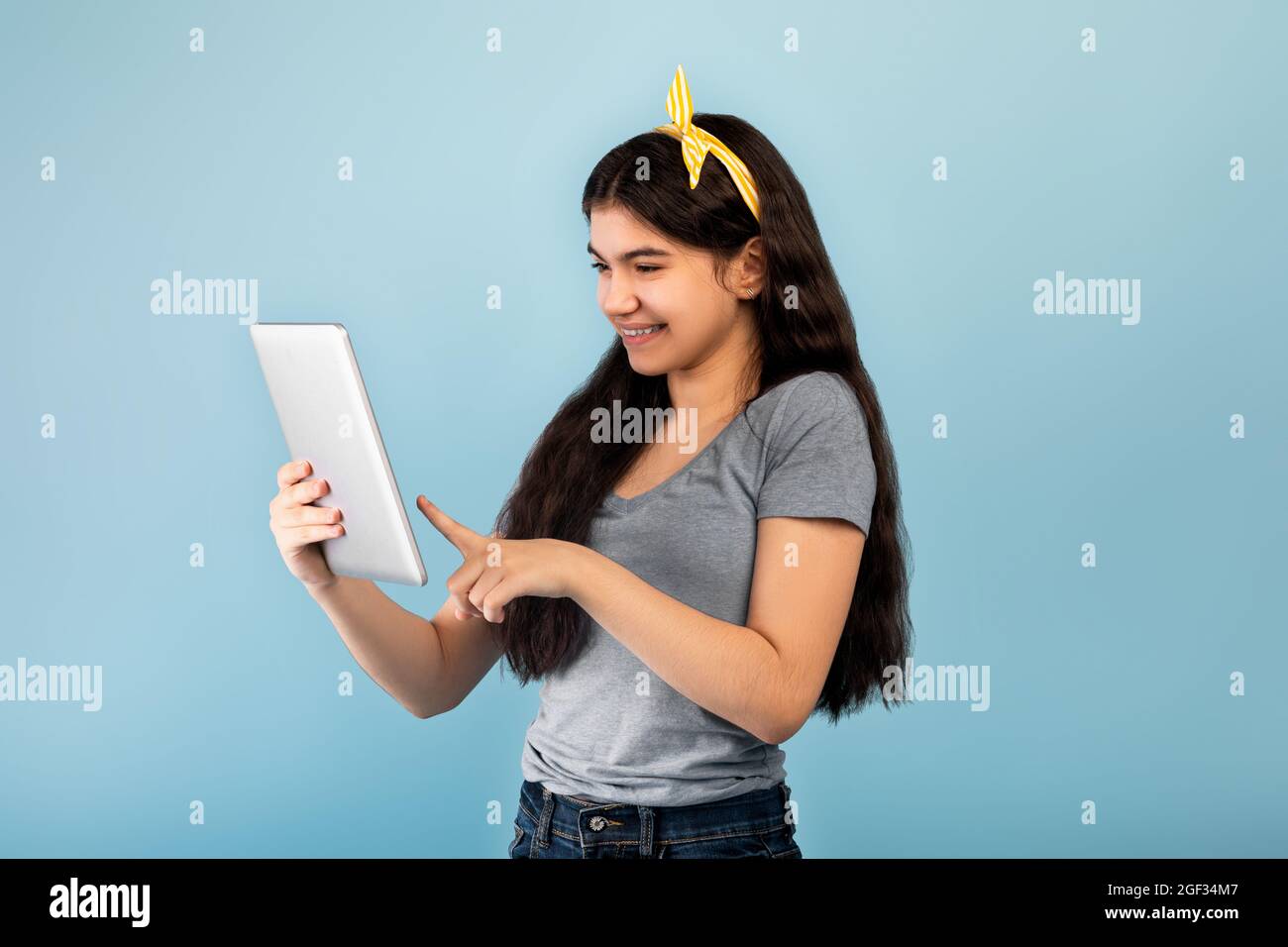 Portrait of cheery Indian teenage girl using modern tablet pc over blue studio background Stock Photo
