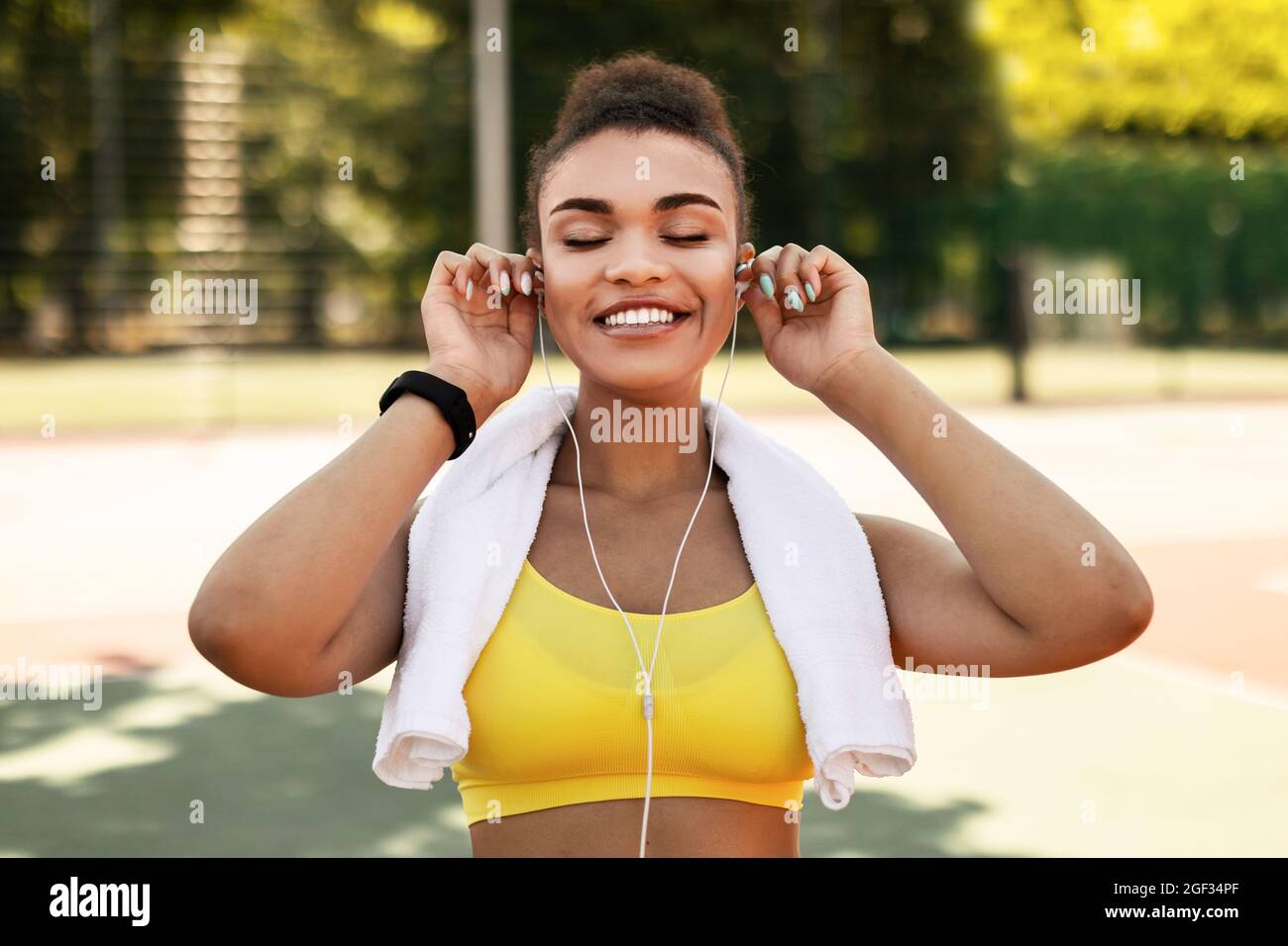 Sporty black woman in yellow sportswear putting on headphones Stock ...
