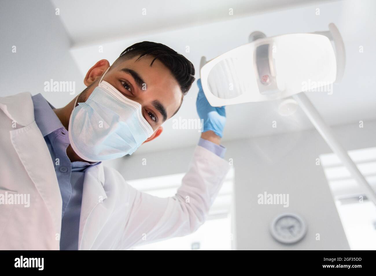 Arab Dentist Turning On Lamp Before Check Up With Patient, Low Angle Stock Photo