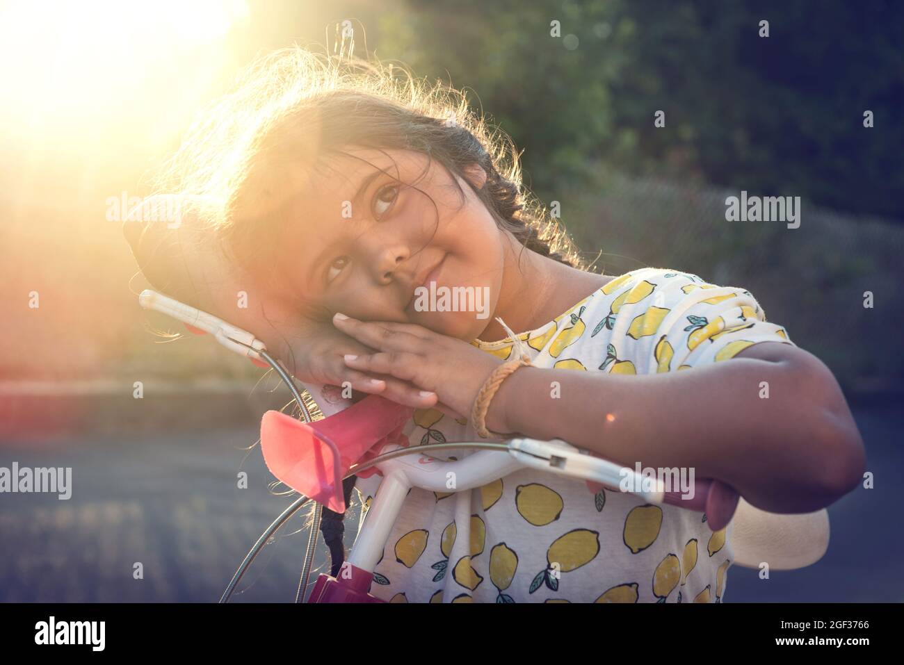 Happy young girl posing in a bicycle outdoors at sunset Stock Photo