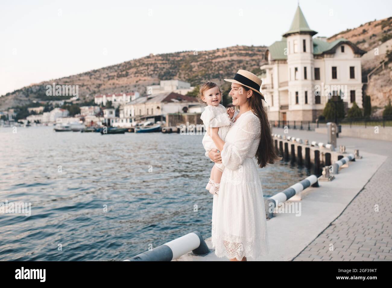 Happy stylish woman hold baby girl 1 year old wear white trendy dress