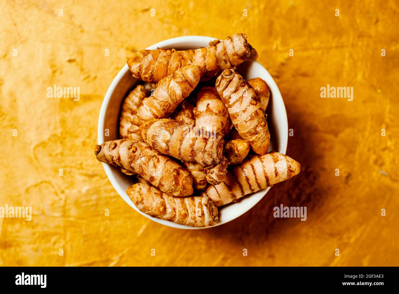 high angle view of some turmeric roots, curcuma longa species, in a ceramic bowl placed on a golden textured surface Stock Photo