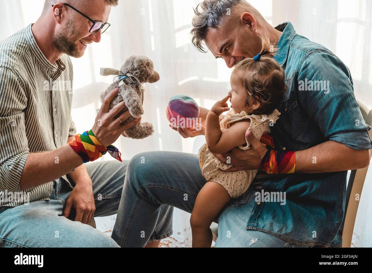 Male gay couple with adopted baby girl at home - Two handsome fathers playing with their daughter - Lgbtq+ family at home - Diversity concept and LGBT Stock Photo