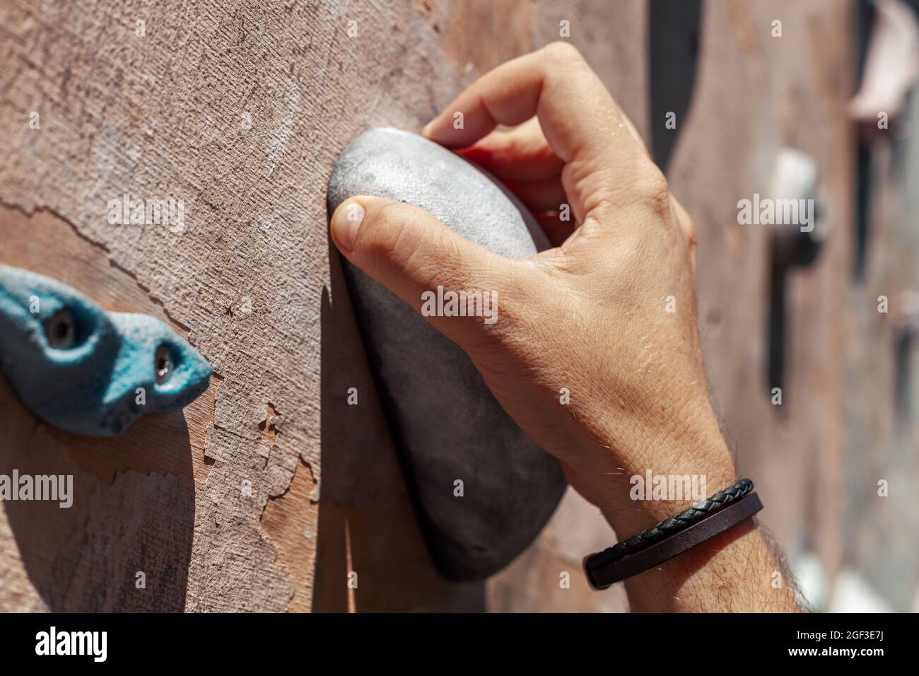 Close-up photo of male hand gripping climbing holds on worn wall outside. Man doing climbing exercise on artificial rock climbing wall at park. Stock Photo