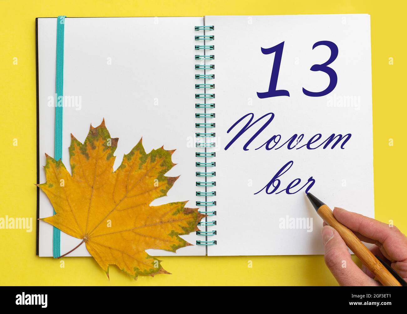 13th day of november. Hand writing the date 13 november in an open notebook with a beautiful natural maple leaf on a yellow background. Autumn month, Stock Photo