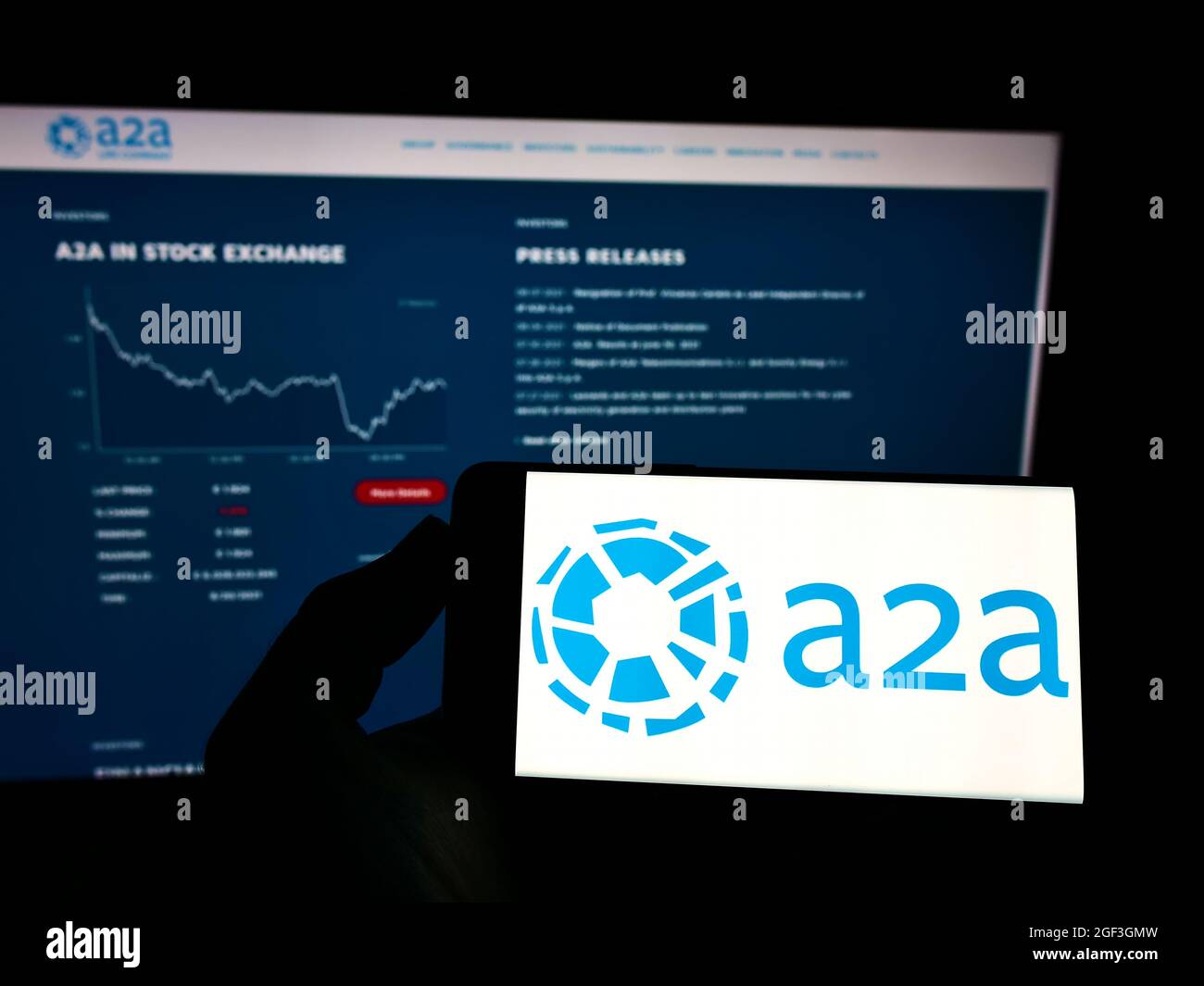 Person holding mobile phone with logo of Italian utility company A2A S.p.A. on screen in front of business web page. Focus on phone display. Stock Photo