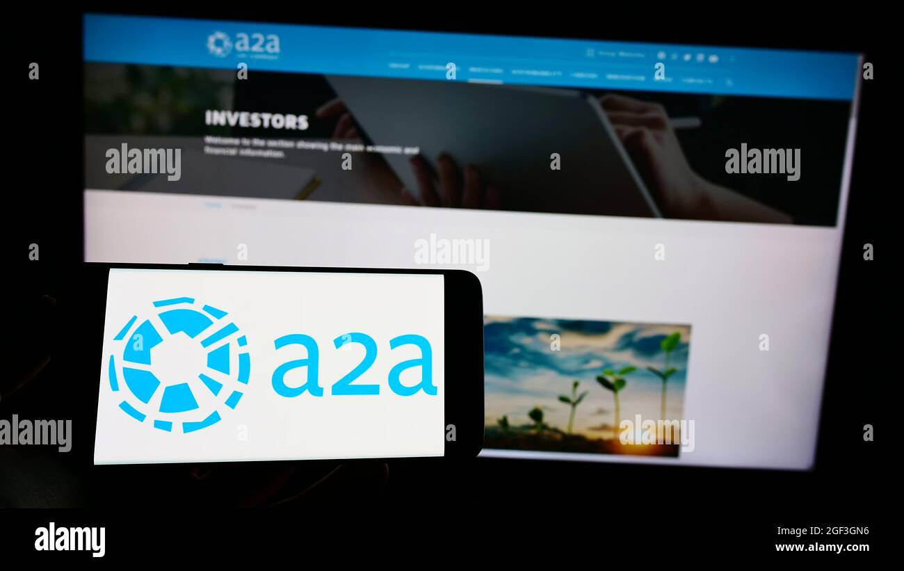 Person holding cellphone with logo of Italian utility company A2A S.p.A. on screen in front of business webpage. Focus on phone display. Stock Photo