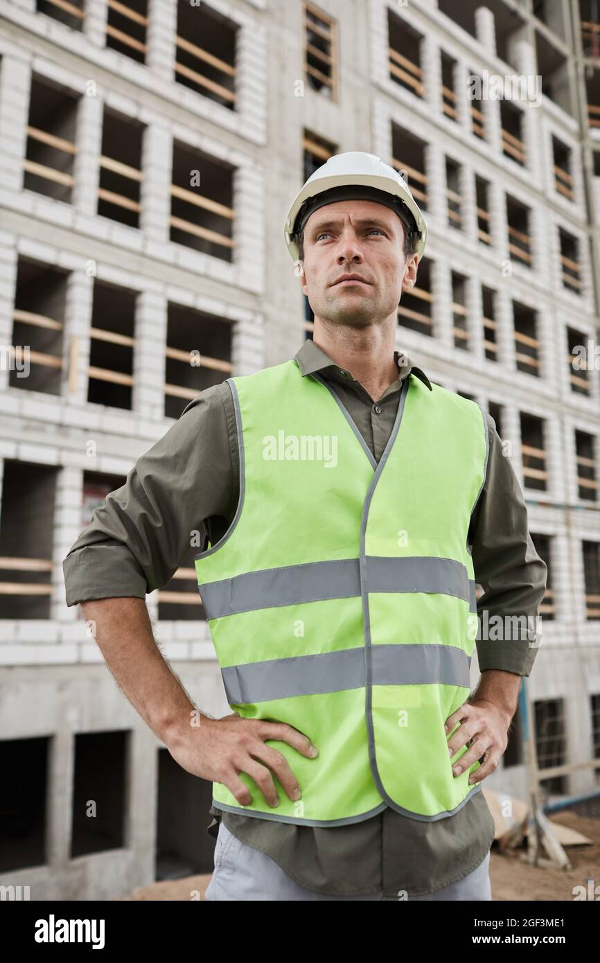 Vertical portrait of young male engineer posing at construction site